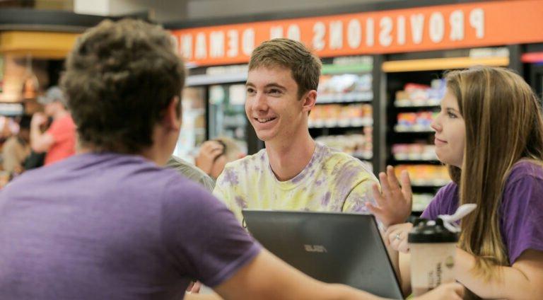 Photo of Three HSU students in focus enjoying conversation at the Moody Center POD.